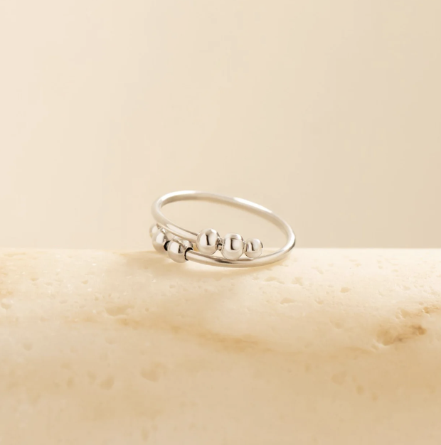 A silver ring with four moveable beads on marble 